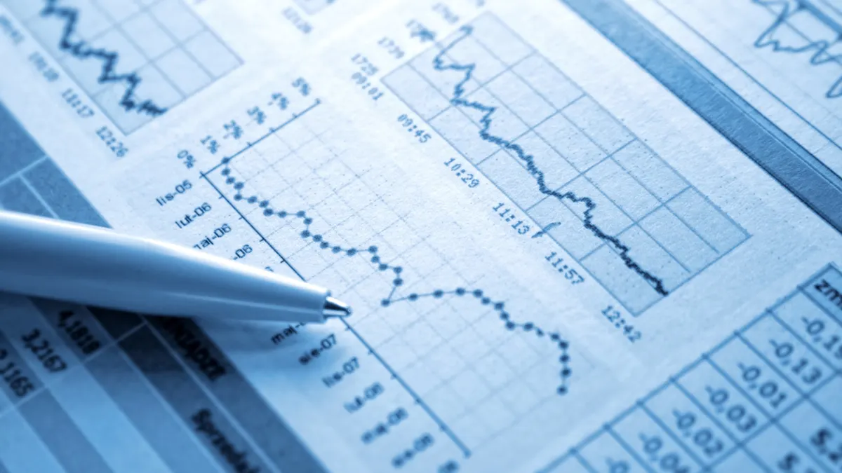 A pen rests atop of a printed page that show charts and graphs depicting spending amounts.