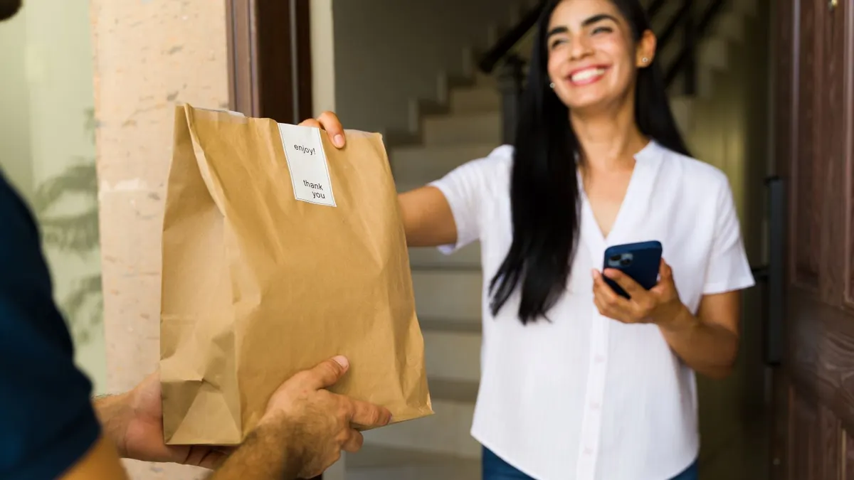 A person holds out a  hand to take a brown bag from a person holding it out.