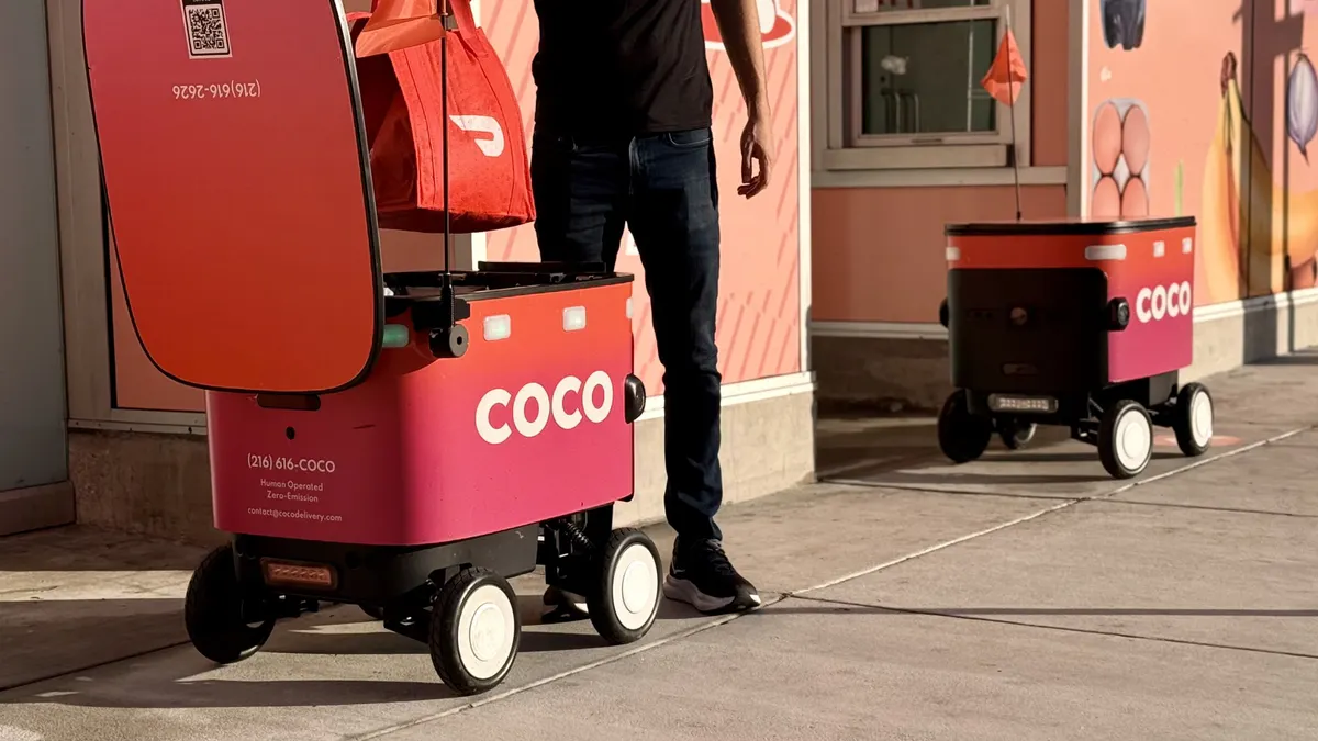 A worker loads a delivery robot with a DoorDash bag