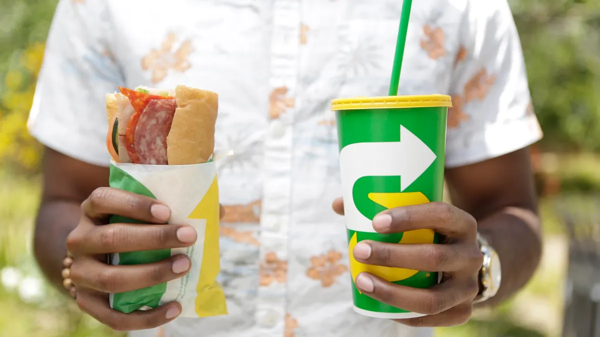 A person holds a Subway sandwich and drink cup