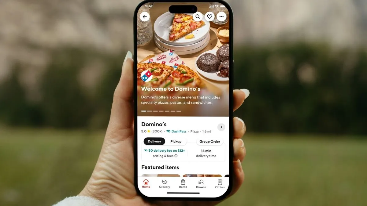 A photograph of a hand holding up a smartphone with it open to Domino's page on DoorDash.