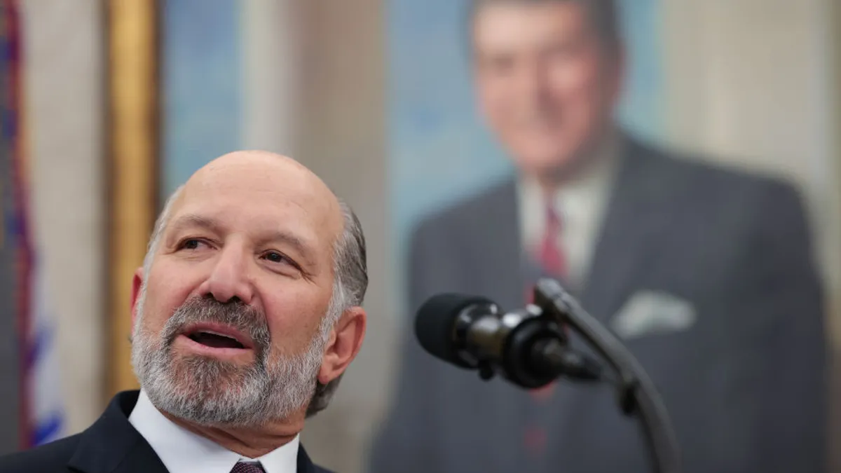 A person speaks at a podium in front of a large, out-of-focus painting.