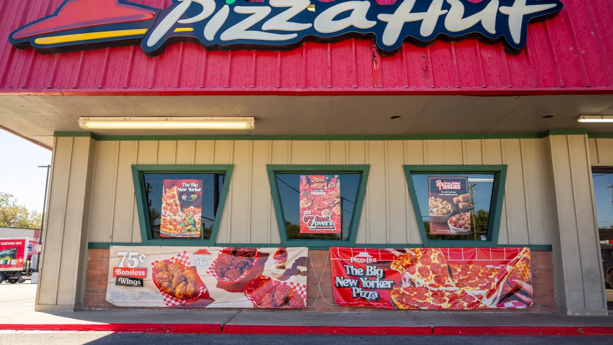 The side view of a Pizza Hut restaurant can be seen, with promotional posters and banners on the windows and walls.