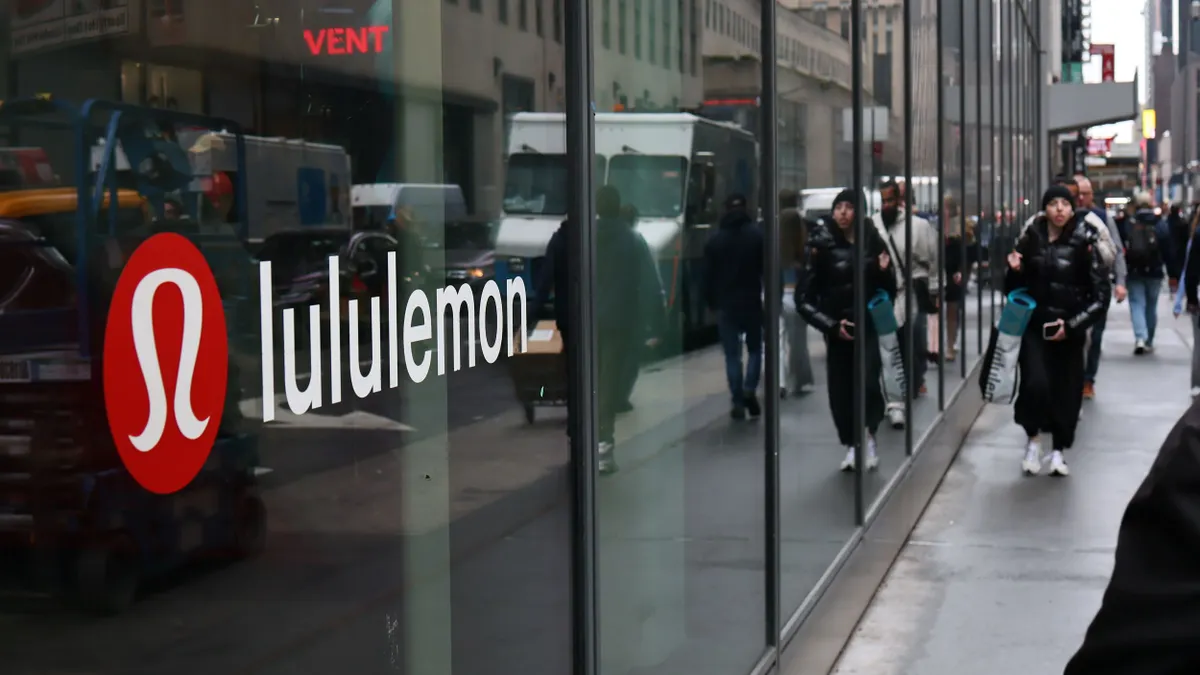 A lululemon logo displayed through a window as people walk by.