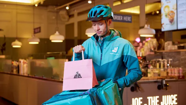 A man in Deliveroo livery loads a Joe and the Juice bag into a delivery bag.