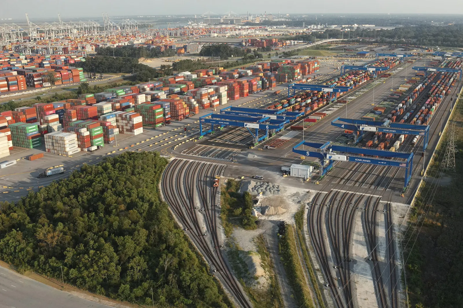An aerial view of shipping containers and rail trackers behind a shipping port.